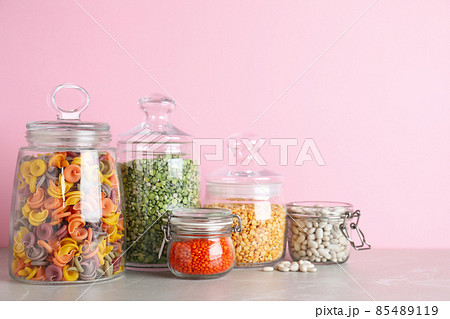 Glass jars with different types of groats and pasta on light grey marble table Glass jars with different types of groats and pasta on light grey marble table 85489119