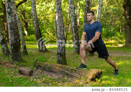 A young enduring athletic athlete is doing stretching in the forest outdoors, around the forest, trees. Active forest, workout outdoor training marathon, trees wellbeing. Adult body running 85489525