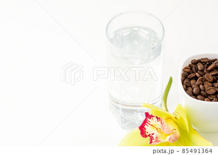 Cup of coffee beans and glass of water with yellow orchid flower against a white background. Cup of coffee beans and glass of water with yellow orchid flower against a white background. 85491364