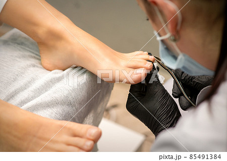 Pedicure master using nail nippers while trimming toenails in a pedicure salon. 85491384