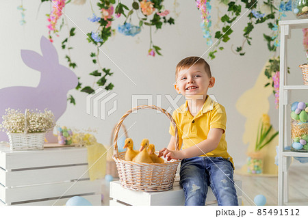 Happy child boy sits near the basket with fluffy ducklings on the wooden box. Easter decoration. Happy child boy sits near the basket with fluffy ducklings on the wooden box. Easter decoration. 85491512
