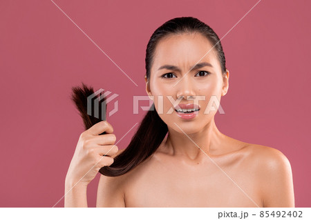 Irritated korean woman holding her ponytail on purple 85492402