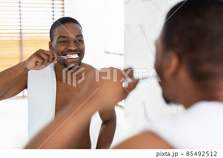 Dental Care. Handsome Shirtless Black Guy Brushing Teeth Near Mirror In Bathroom Dental Care. Handsome Shirtless Black Guy Brushing Teeth Near Mirror In Bathroom 85492512