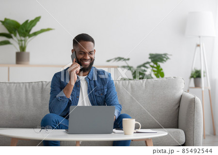 Happy busy millennial african american businessman freelancer with beard looks at pc, call to client by phone 85492544