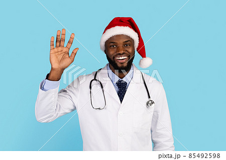 Smiling Black Doctor In Santa Hat Waving Hand At Camera Smiling Black Doctor In Santa Hat Waving Hand At Camera 85492598