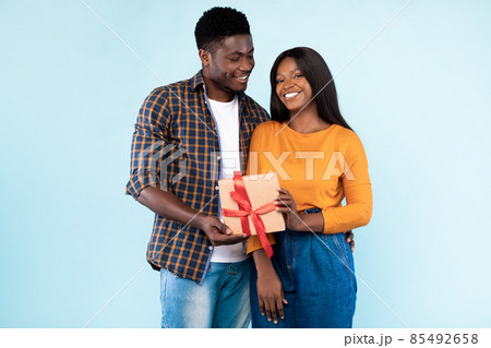 Happy black couple holding gift box at blue studio Happy black couple holding gift box at blue studio 85492658