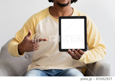 Black Guy Pointing At Digital Tablet With Blank Screen, Sitting In Armchair 85492957