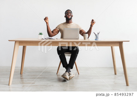 Excited young black man gesturing YES in front of laptop, celebrating success or achievement, sitting at desk in office 85493297