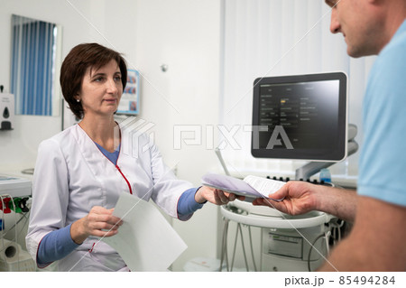 Healthcare and medicine theme. Female general practitioner will see medical tests during health examination of male patient in clinic office. Medical worker in ultrasound diagnostic room with patient 85494284