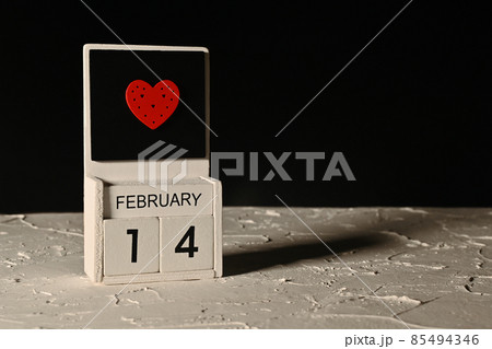 Valentine's Day with a wooden block calendar and a heart. On a white concrete floor on a black background. copy space 85494346
