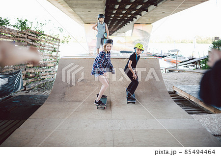 Boys girls friends have fun together howling during skateboarding training, riding and doing tricks on half pipe in skate park. Youth, togetherness and friendship concept. Sports club for children Boys girls friends have fun together howling during skateboarding training, riding and doing tricks on half pipe in skate park. Youth, togetherness and friendship concept. Sports club for children 85494464