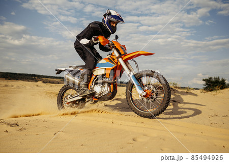 Professional motocross rider driving on sand dune Professional motocross rider driving on sand dune 85494926