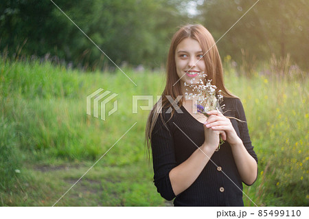 Happy young woman in a field on nature holds wildflowers in her hands and smiles. Happy young woman in a field on nature holds wildflowers in her hands and smiles. 85499110