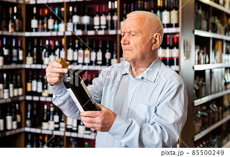 Elderly man chooses red wine in a liquor store 85500249