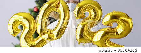 Woman in protective suit and mask holds numbers 2022 against background of Christmas tree Woman in protective suit and mask holds numbers 2022 against background of Christmas tree 85504239