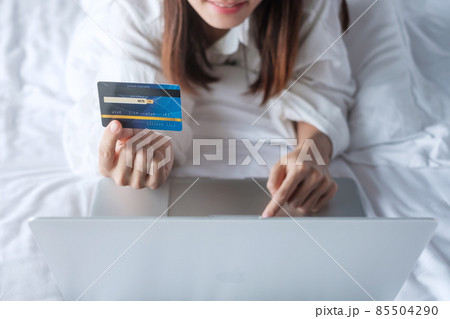 woman using computer laptop and credit card for online shopping while making order on bed in morning at home. technology, ecommerce, digital banking online payment and apartment living concept 85504290