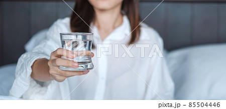 Happy woman holding water glass, female drinking pure water on bed at home. Healthy, Refreshment, lifestyle concept Happy woman holding water glass, female drinking pure water on bed at home. Healthy, Refreshment, lifestyle concept 85504446