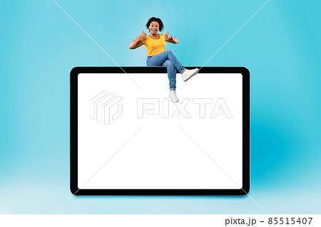 Cool young black woman sitting on giant cellphone, showing thumb up gesture, recommending new app or website, mockup 85515407