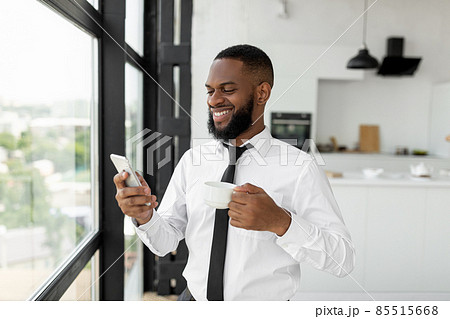 Black guy texting on his smartphone drinking coffee Black guy texting on his smartphone drinking coffee 85515668