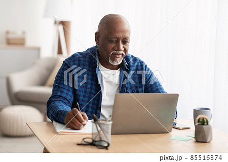 Senior Black Man Using Laptop Taking Notes Working At Home Senior Black Man Using Laptop Taking Notes Working At Home 85516374