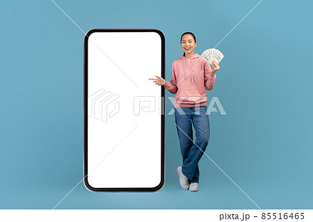Cheerful asian woman with bunch of dollars and big smartphone Cheerful asian woman with bunch of dollars and big smartphone 85516465