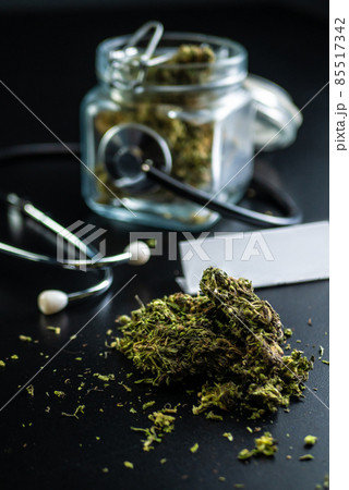 Dry medical cannabis in a jar with a stethoscope on a black background Dry medical cannabis in a jar with a stethoscope on a black background 85517342