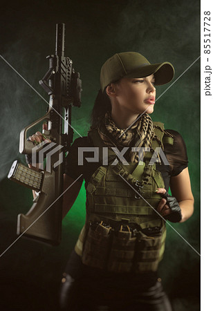 the girl in military special clothes posing with a gun in his hands on a dark background in the haze 85517728