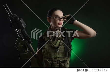 the girl in military special clothes posing with a gun in his hands on a dark background in the haze 85517735