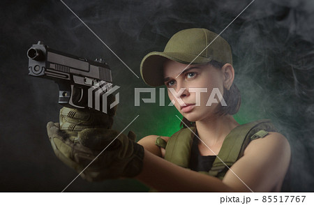 the girl in military special clothes posing with a gun in his hands on a dark background in the haze 85517767