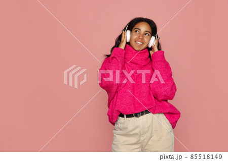 Half-length portrait of young pretty dark skinned girl in warm knitted sweater isolated on pink background. Half-length portrait of young pretty dark skinned girl in warm knitted sweater isolated on pink background. 85518149