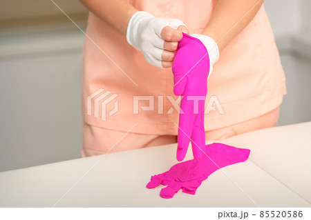 Hands of beautician put on rubber pink gloves prepare to receive clients. Hands of beautician put on rubber pink gloves prepare to receive clients. 85520586