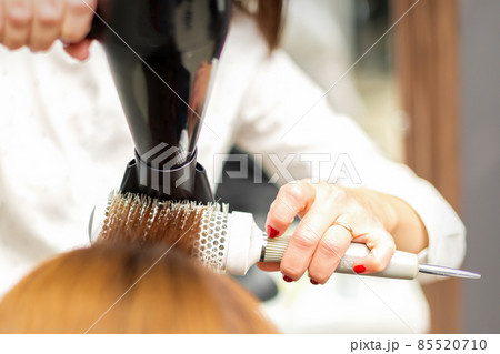 A professional hairdresser is drying long red hair with a hair dryer and round brush, close up. A professional hairdresser is drying long red hair with a hair dryer and round brush, close up. 85520710