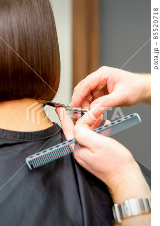 The hairdresser cuts the hair of a brunette woman. Hairstylist is cutting the hair of female client in a professional hair salon, close up. The hairdresser cuts the hair of a brunette woman. Hairstylist is cutting the hair of female client in a professional hair salon, close up. 85520718