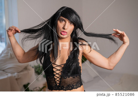 A homosexual guy in black lace underwear and a wig grimaces at the camera. 85521086