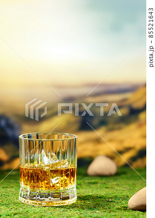 Glass of smoky whiskey placed on green moss with defocused mountain landscape on background Glass of smoky whiskey placed on green moss with defocused mountain landscape on background 85521643