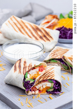 Chicken wraps with red cabbage, avocado, tomato, lettuce, cheddar cheese, on a wooden tray Chicken wraps with red cabbage, avocado, tomato, lettuce, cheddar cheese, on a wooden tray 85522210