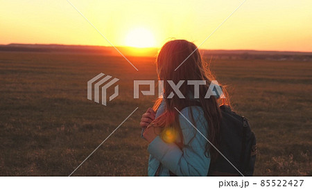 A girl traveler walks with a backpack on her back and smiles at the sunset in the sky. A teenager on a camping trip on vacation. Childhood in search of adventure from morning to dawn. Love for the 85522427