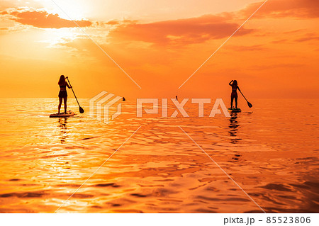 Travelers on stand up paddle board at quiet sea with sunset or sunrise. Girls on Red Paddle sup board and sunset 85523806