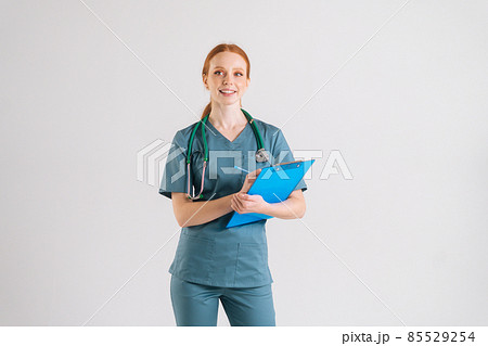 Portrait of cheerful young adult woman nurse in medical uniform writing prescription on clipboard, fills out medical history, looking at camera. Portrait of cheerful young adult woman nurse in medical uniform writing prescription on clipboard, fills out medical history, looking at camera. 85529254