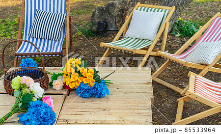 Beautiful artificial bouquets of various colors placed on wooden table among deck chairs in garden. Multi-colored artificial flowers adorn the wooden table for beautiful and relaxing. Selective focus. Beautiful artificial bouquets of various colors placed on wooden table among deck chairs in garden. Multi-colored artificial flowers adorn the wooden table for beautiful and relaxing. Selective focus. 85533964