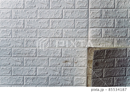 The wallpaper begins to peel off. Old white bricks wallpaper peeled off from the wall inside the room due to moisture or poor quality gluing. Repair and construction services concept. Selective Focus. 85534187