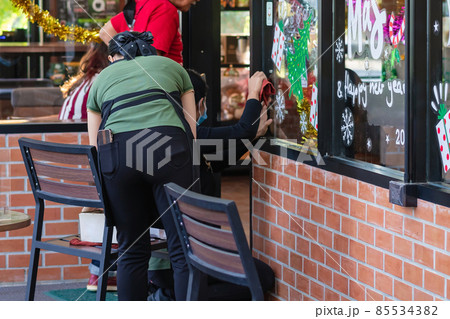 Asian women decorate beautiful stickers on window glass in front of cafe to welcome Christmas and New Year. Prepare to decorate the storefront to be beautiful during the important holidays of year. Asian women decorate beautiful stickers on window glass in front of cafe to welcome Christmas and New Year. Prepare to decorate the storefront to be beautiful during the important holidays of year. 85534382