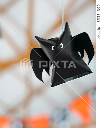 Origami bat made of black paper hanging on a rope for Halloween decorations. Dark paper ghost Halloween party concept origami paper bat. The figure of black paper bat flying over room. Space for text. Origami bat made of black paper hanging on a rope for Halloween decorations. Dark paper ghost Halloween party concept origami paper bat. The figure of black paper bat flying over room. Space for text. 85534399
