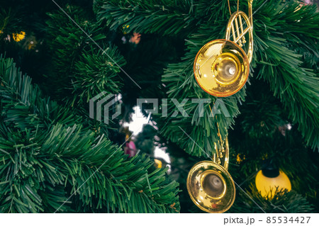 Shiny horns ornament or small golden euphonium hanging on pine tree. Stylish christmas decorations. Christmas and New Year display for celebration,carnival,festival design concept. Selective focus. Shiny horns ornament or small golden euphonium hanging on pine tree. Stylish christmas decorations. Christmas and New Year display for celebration,carnival,festival design concept. Selective focus. 85534427