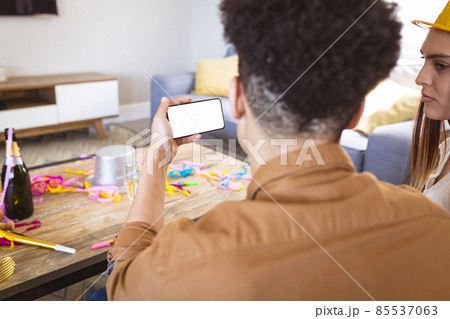 Young man sharing blank smart phone screen with girlfriend at home during party Young man sharing blank smart phone screen with girlfriend at home during party 85537063