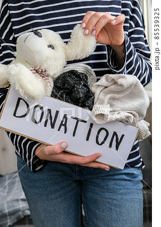 Female volunteer holding donation box with old used toys and clothes indoors. Happy Charity. Unrecognizable woman holding box with clothes in it. close-up. Clothing donation. Female volunteer holding donation box with old used toys and clothes indoors. Happy Charity. Unrecognizable woman holding box with clothes in it. close-up. Clothing donation. 85539325