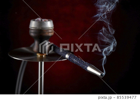 Smoke streaming from the mouthpiece of a modern hookah, on a beautiful dark background. Smoking shisha. 85539477