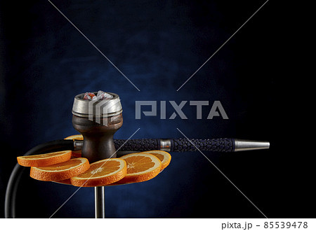 Modern hookah decorated with orange slices on a blurry dark blue background. The culture of serving shisha. Modern hookah decorated with orange slices on a blurry dark blue background. The culture of serving shisha. 85539478