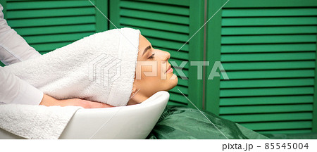 Hairdresser wraps hair of a young caucasian woman in a white towel after washing head in the hairdressing salon. 85545004