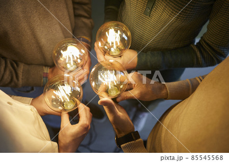Team of four intelligent people together holding bright, shining, glowing Edison light bulbs as symbol of implementing innovations and developing modern, creative, clever ideas, close up, closeup shot 85545568